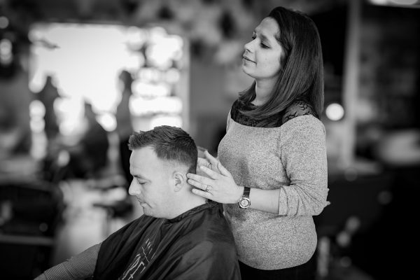 une coiffeuse repositionne la tête de son client